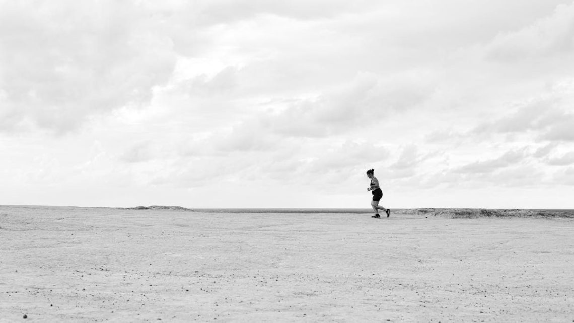A person running across an expansive desert under a cloudy sky in Natal, Brazil.